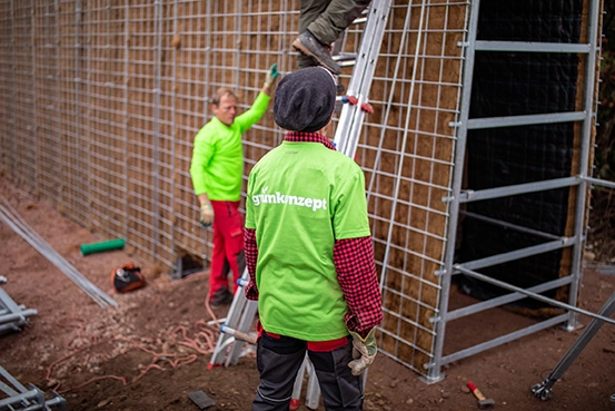 Arbeiter mit Grünkonzept T-shirt steht vor gerade erbauender Lärmschutzwand